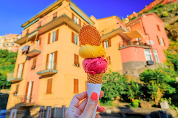 Hand with gelato and view of traditional houses in Manarola, Cinque Terre, Italy