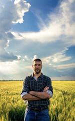 Portrait of young farmer standing in a green wheat field looking at camera.