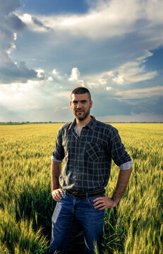 Portrait of young farmer standing in a green wheat field looking at camera.