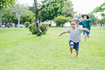 Fototapeta premium Happy girl running on green grass in the park Cheerful children in the meadow in the park under the sunlight. Child playing on spring grass, young woman's sprint at sunset in evening backyard.