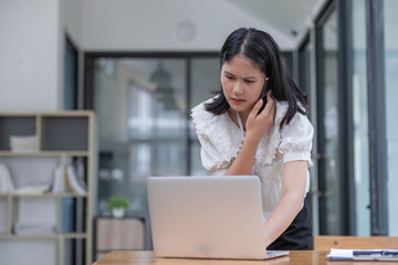 Portrait of smiling young Asian female manager working remotely, holding paper and reading financial document, talking on mobile phone standing at desk at home office