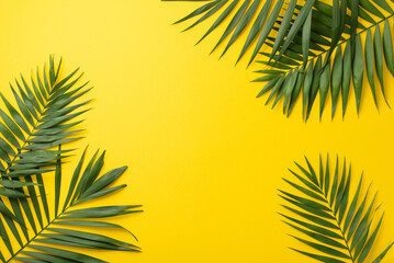 Fototapeta na wymiar Escaping to paradise. Overhead view of natural palm leaves on a vivid yellow backdrop with ample space for text or promotional messaging