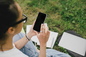Young woman student studying using her books, laptop and notebook, sitting on grass.