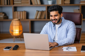 Fototapeta na wymiar Portrait Of Smiling Middle Eastern Male Manager Working On Laptop Computer In Modern Office, Cheerful Guy Sitting At Desk And Using Pc, Looking At Screen Typing On Keyboard, Enjoying Remote Job