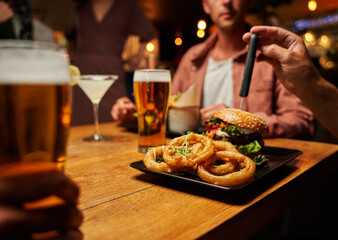 Close-up of young multiracial friends in casual clothing enjoying fast food and drinks at restaurant