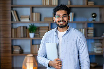 Smiling IT worker in blue shirt look at camera holding laptop at office. concept of remote and freelance work. Young smiling modern successful man in glasses