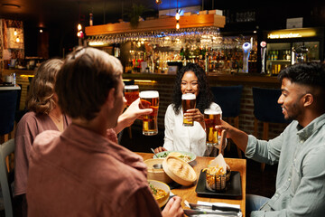 Happy young multiracial group of friends in casual clothing sitting with food and drinks at bar
