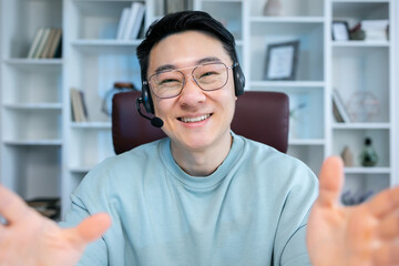 Young happy asian man talking on video conference call greeting waving hand using laptop at modern home office. Remote distant online communication technologies concept.