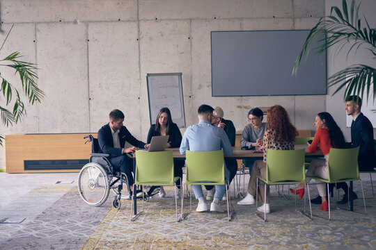 A diverse group of business professionals, including an person with a disability, gathered at a modern office for a productive and inclusive meeting.