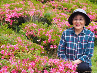 鮮やかなツツジの花と記念撮影する笑顔のシニア女性