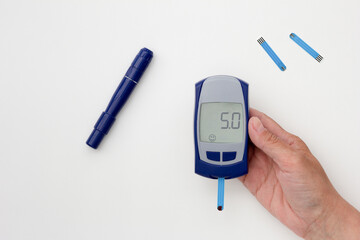Top view of cropped woman hand holding glucometer with 5.0 result on display with blooded test strip inside, lancet and test strips on white background