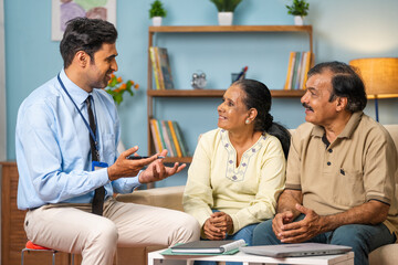 Professional Indian banker explaining about insurance policy to senior couple at home - concept of...