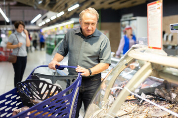 Adult male shopper chooses salted and dried fish in the fish section of supermarket