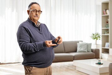Mature man pricking finger with a medical device at home in a living room