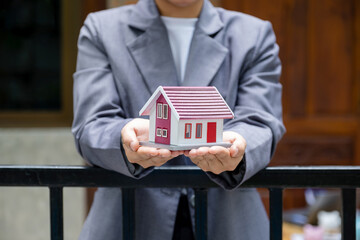 Real estate agent hands holding the home model stand in front of the home wall background