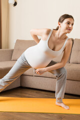 Fototapeta na wymiar Pregnant woman exercising on orange mat in room. Pregnancy Yoga and Fitness concept at coronavirus time