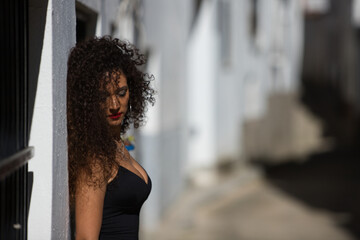 Obraz premium beautiful brunette woman with curly hair and elegant black dress is visiting a city of andalusia in the south of Spain. The city with white walls and typical mediterranean style.