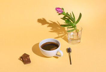 Time for a break with a cup of black coffee and chocolate. A view of a pink flower in a glass....