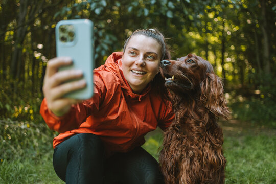 Happy caucasian girl hiker hiker takes a selfie with her cute Irish Setter dog on a walk in a summer forest, adventure travel and discovery