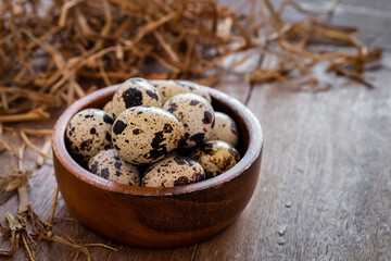 Quail eggs in wooden bowl and dry straw on old table