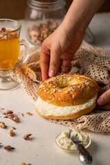 mano de mujer sosteniendo un pan partido por la mitad con queso crema y una bebida caliente