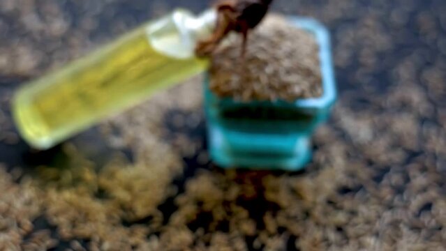 Dolly shot of jeera zeera oil in a bottle glass bowl on a black glowing surface with raw zeera cumin seeds (Cuminum cyminum). HD footage 24 FPS.