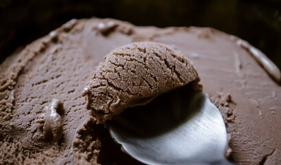 Chocolate ice cream in a spoon close-up. Delicious chocolate ice cream on a dark background. In a...