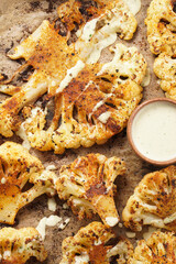 A close-up photo of oven roasted thin slices of white cauliflower seasoned with paprika and black pepper, with hearty tahini sauce. flat lay, top view
