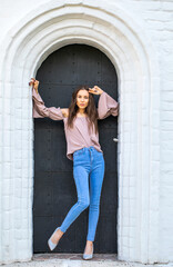 Fototapeta na wymiar Portrait of a young beautiful brunette girl in blue jeans posing in a stone arch