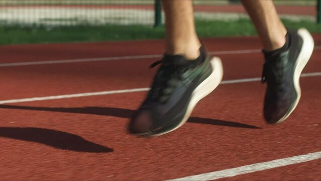 Male spindle muscled legs in black sneakers running along one lane of a red athletic track, tracking close up shot.