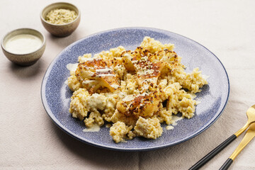 A blue plate with cooked millet and roasted cauliflower with paprika and black pepper seasoning, tahini dressing, on linen table cloth, a delicious gluten free vegan meal