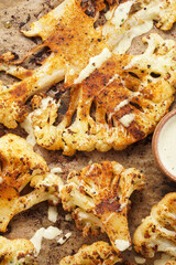 A close-up photo of oven roasted thin slices of white cauliflower seasoned with paprika and black pepper, with hearty tahini sauce. flat lay, top view
