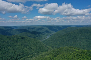 Fototapeta na wymiar River Cutting Through Green Mountains under a Blue Sky with Puffy White Clouds