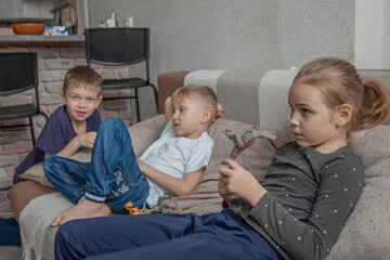 two little boys and a little girl are watching TV together, bored. Children are idle and do not know what to do with themselves