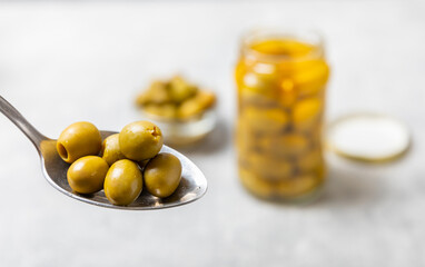 Close-up of olives in a spoon and glass jar on the kitchen table. pitted green olives in jar.Pickled olives in glass jar. On a wooden background.Marinaded olives. Space for text.Space for copy. 
