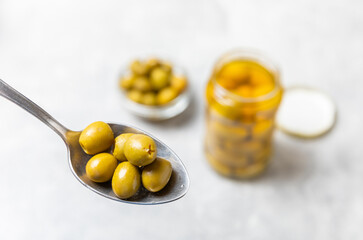 Close-up of olives in a spoon and glass jar on the kitchen table. pitted green olives in jar.Pickled olives in glass jar. On a wooden background.Marinaded olives. Space for text.Space for copy. 