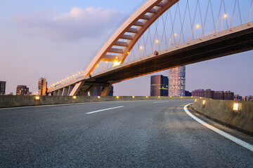 Fototapeta na wymiar Asphalt road and bridge with city skyline at sunset