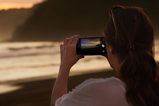 Mockup image. Woman use cell phone on beach, summer holiday. Woman holding mobile phone with blank desktop screen on the beach. Mobile phone in female hand on the background of the resort beach