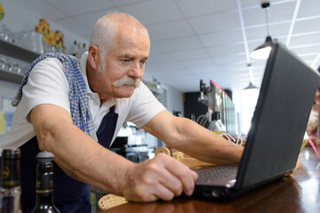 senior male barista looking at laptop