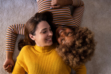 Top view of lovely multiracial lesbian couple lying on a carpet looking aat each other. Two...