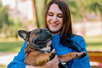 the young owner is holding a small cute French bulldog in her arms who is smiling a portrait of an animal in nature
