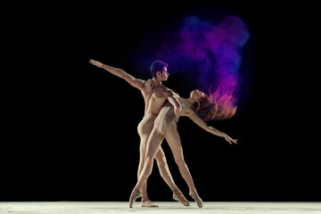 Graceful, beautiful couple, man and woman, ballet dancers performing against black studio background with colorful power explosion. Concept of art, festival, beauty of dance, inspiration, youth