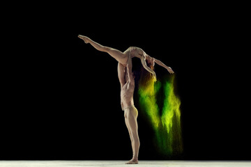 Fototapeta na wymiar Attractive, talented, young man and woman, ballet dancers making colorful performance with powder explosion over black studio background. Concept of art, festival, beauty of dance, inspiration, youth