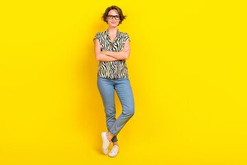 Full length photo of confident business lady hold folded arms wear specs print blouse jeans shoes isolated yellow color background