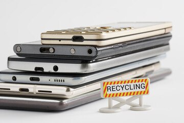 Lots of old smartphones next to the "Recycling" sign. The concept of recycling obsolete gadgets. White background. Photo