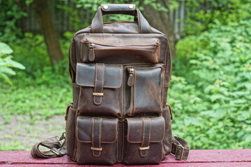 modern comfortable classic brown leather backpack with iron fittings stands on a brown wooden table outdoors during the day
