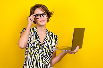 Portrait of clever positive woman short haircut wear striped blouse touching glasses hold laptop isolated on yellow color background