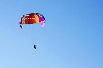Tourists fly on a bright paraglider against the blue sky in the summer on a sunny day. Beach holidays, tourist marine entertainment
