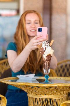 Redhead woman taking a picture of an ice cream in a terrace