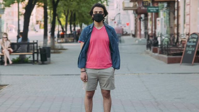 Zoom-out time lapse portrait of Arab guy wearing medical face mask standing in busy street surviving covid-19 pandemic. City life and infection outbreak concept.